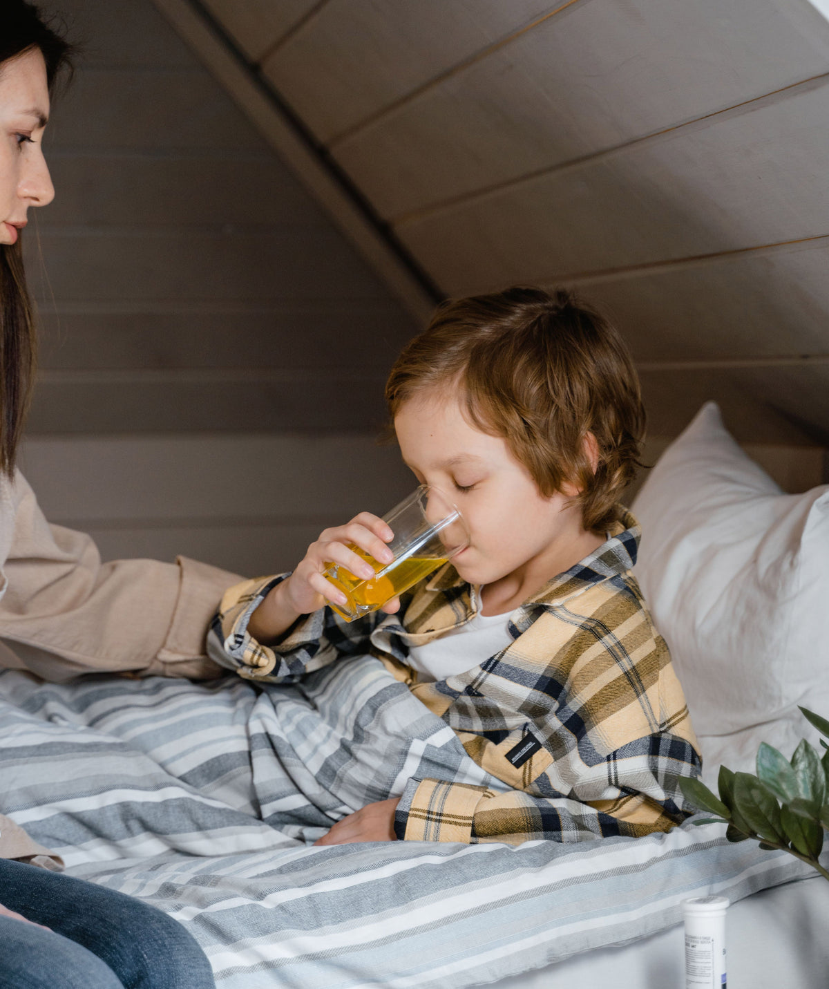 Young child sitting up in bed drinking from a small glass with a parent nearby